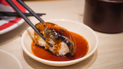 Close up photo of someone dipping sushi in soy sauce using chopsticks on Japanese Restaurant....