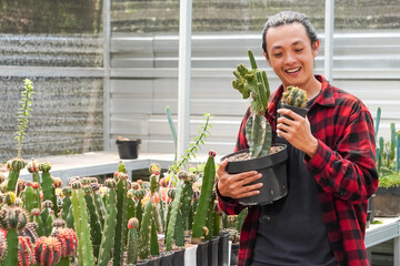 Handsome happy long haired asian man cactus gardener in red flannel holds a cactus flower in a...