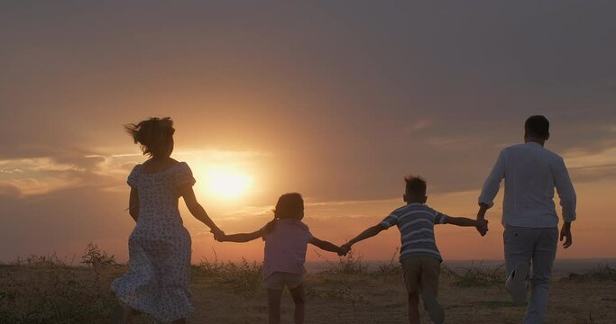 Happy family run in the park at sunset. Happy family running towards the sun holding hands. Family have fun, joy in nature. Healthy young family at sunset. Concept of happy people in nature