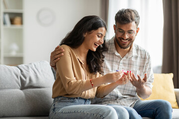 Happy indian spouses holding positive pregnancy test, sitting on couch at home together, couple celebrating awaiting baby, copy space - obrazy, fototapety, plakaty