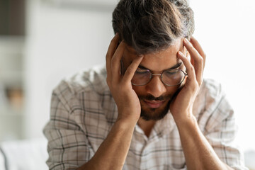 Young indian man suffering from migraine, feeling unwell, touching head with closed eyes, suffering...