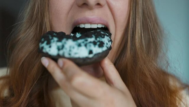 Close up portrait of a hungry 30s woman eating donuts with white frosting. Eating donut when takeout and delivery. Fast food takeaway back home. High quality FullHD footage. High quality FullHD