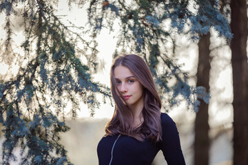 A girl stands near a blue spruce in an autumn park.