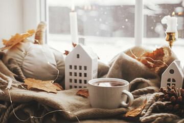 Cozy Autumn. Warm cup of tea, stylish pumpkin pillows, fall leaves, candle, lights and cute...