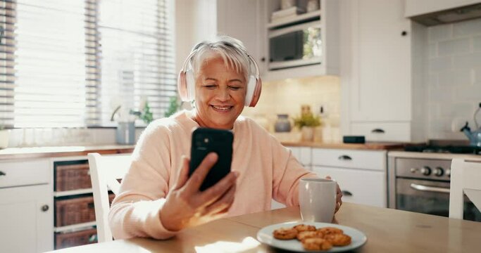 Headphones, Phone And Senior Woman In The Kitchen Watching Funny, Comic Or Comedy Video On Social Media. Happy, Laugh And Elderly Female Person Reading Post Online With Cellphone, Coffee And Biscuits