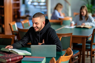 Happy young student using notebook and books and learning in the university library