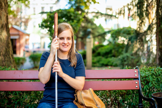 Close-up of a visually impaired woman holding a white cane and sitting on a bench in the city