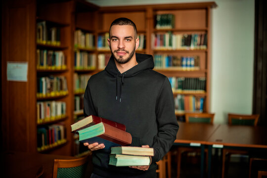Young man standing in the university library and holding books in his hand