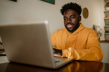 A serious interracial remote worker is typing on the laptop while working remotely from home at...