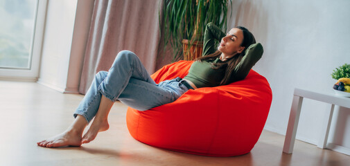 Fototapeta na wymiar Beautiful young brunette woman in casual clothes sitting on bean bag chair at home and relax, rest, thinking and meditating
