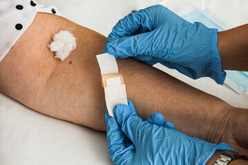 Moment of a doctor preparing to apply an adhesive bandage to an elderly woman after receiving a ba virus vaccine.2.86 - obrazy, fototapety, plakaty