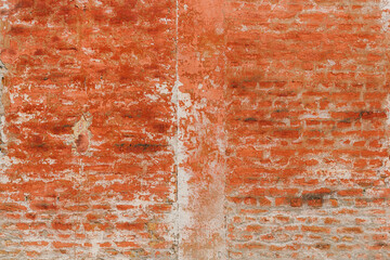 Old brick wall featuring peeling red paint and weathered old mortar as background with unique texture and pattern