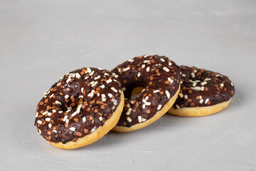 Three donuts covered with chocolate glaze on gray background