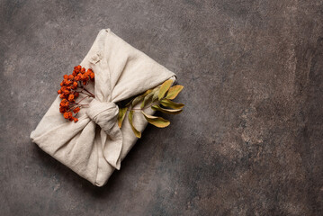 Autumn gift with rowan wrapped in fabric on brown rustic background. A traditional furoshiki gift. Top view, flat lay, copy space.