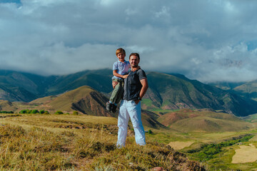 Fototapeta na wymiar Happy boy sitting in his father's arms on mountains background