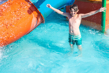 a child in swimming shorts stands in a blue pool under splashes of water, in a children's water...
