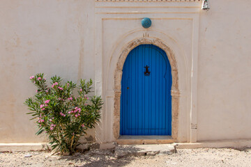 Traditional blue door with pattern tiles and pink flowers, Hara Sghira Er Riadh - Djerbahood in Tunisia