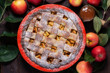 Traditional holiday apple pie with cinnamon and cardamom in a ceramic form, apples and apple branches.