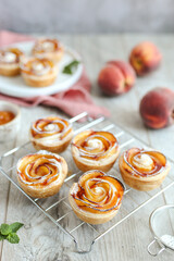 Nectarine Roses made of puff pastry, on a white plate. Buttery, flaky and crispy puff pastry rolls with layers of flavorful nectarine slices. Pink napkin.
