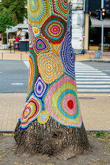 Colorful crochet knit on tree trunk in Kyiv, Ukraine. Street art goes by different names, graffiti knitting, yarn bombing. Abstract background of knitted rugs with a multicolored circles pattern