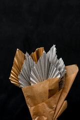 Selective focus of dried leaves in silver and gold colors wrapped in kraft paper on black studio background