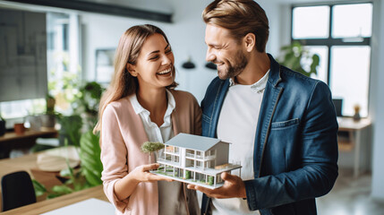 happy couple in the real estate offices at the office holding house model in hands