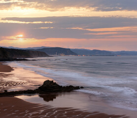 Fototapeta na wymiar Twilight ocean rocky coast landscape with sky reflection on wet sand of beach (Spain).