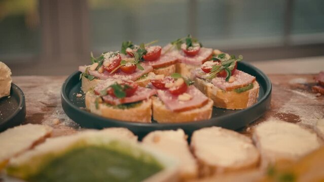 Close up of beautifully put bruschettas with ham, parmesan and cherry tomatoes on a small plate. High quality 4k footage