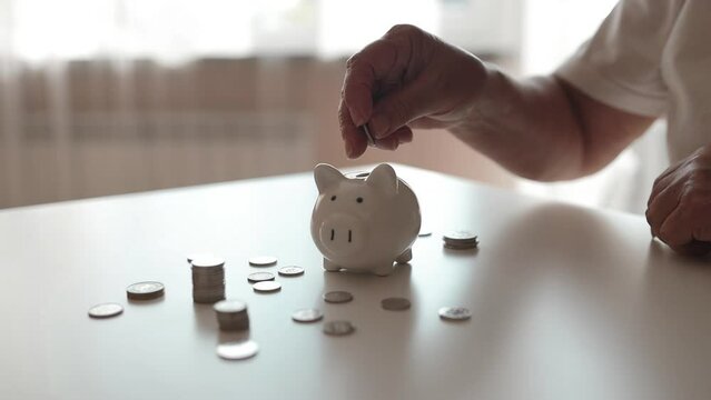 Senior 50s woman hand putting money coin into piggy for saving money wealth and financial concept. High quality FullHD footage