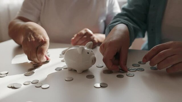 Senior 50s woman and girl hand putting money coin into piggy for saving money wealth and financial concept. High quality FullHD footage
