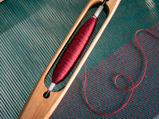 Interweaving of green warp threads and red weft threads, close up. Weaving loom, yarn and boat shuttle - obrazy, fototapety, plakaty