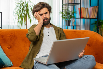 Displeased Middle eastern man use laptop notebook typing browsing working, loses becoming surprised...