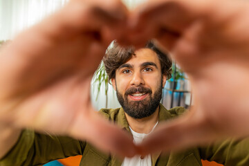 I love you. Happy middle eastern man at home living room couch makes symbol of love showing heart sign to camera express romantic feelings express sincere positive feelings. Charity gratitude donation