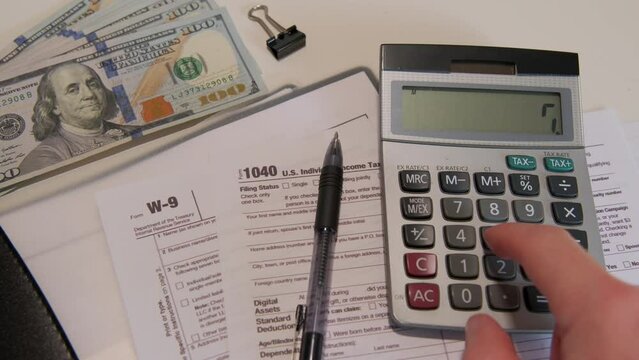 calculate the amount on a calculator 1040 and W9 individual tax form are placed on desk of American citizen.