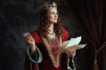 happy medieval queen in red dress with parchment and crown