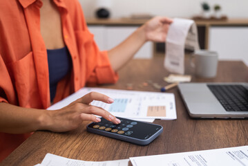 Smartphone Finance: With a laptop on the desk, a woman skillfully calculates household expenditures on her smartphone.