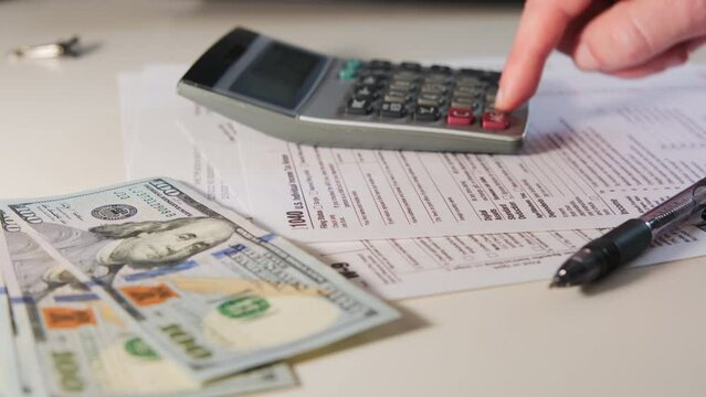 Close up shot of calculate the amount on a calculator 1040 and W9 individual tax form are placed on desk of American citizen. 