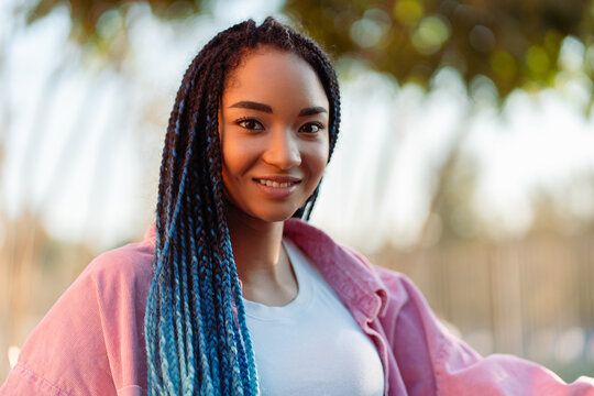 Portrait authentic smiling African American young woman with blue braids outdoors looking at camera