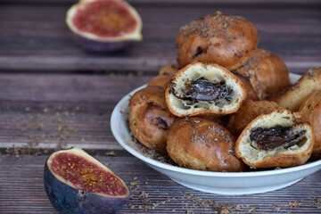 Delicious homemade profiteroles cakes with cocoa cream filling and chocolate chips. Choux pastry, cream puffs halved on plate, fig halves on wooden table background. 