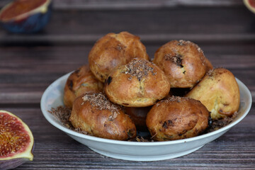 Delicious homemade profiteroles cakes with cocoa cream filling and chocolate chips. Choux pastry, cream puffs on plate, fig halves on wooden table background. 