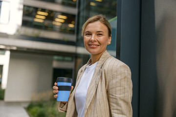 Female manager going to work while drinking coffee on office building background. High quality photo