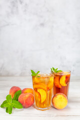 Peach ice tea in a glass with mint on white wooden table.
