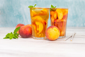 Peach ice tea in a glass with mint on white wooden table.
