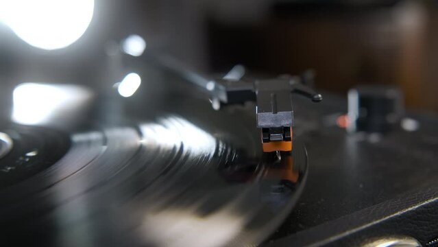 Close up footage of hands placing the vintage turntable on a spinning vinyl record and light in the background