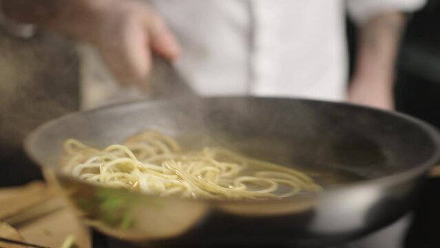 Chef cooks spaghetti pasta in a frying pan with fried salmon in a restaurant kitchen