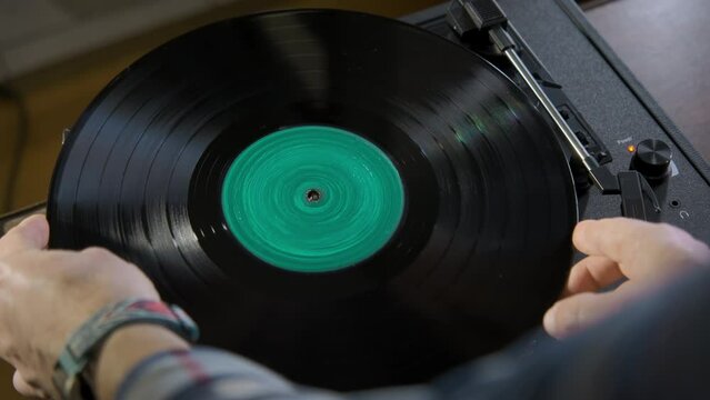 Top shot of hands placing the vintage turntable green color screen in center on a spinning vinyl record. 