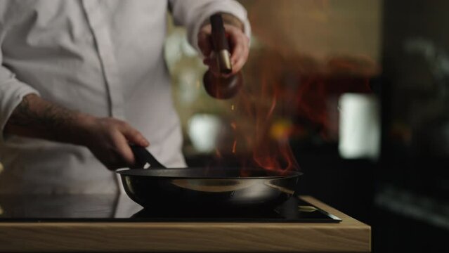 Chef doing flambe to dish in pan with large fire flame in sliced vegetables