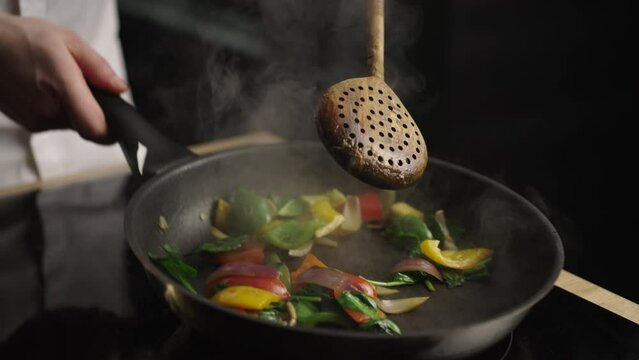 Slow-motion shot of a man cooking vegetables in frying pan. He is mixing vegetables with a spoon. Close-up view