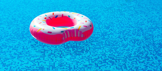 inflatable ring in the form of a donut with pink glaze in the pool in the bright sun. summer vacation, tan