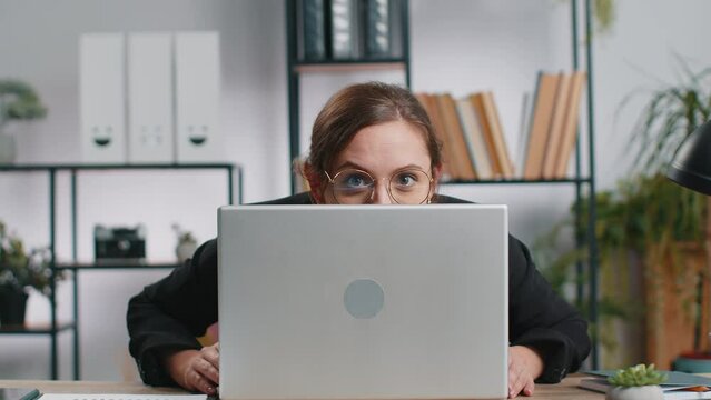 Caucasian business woman hiding behind laptop computer making funny face, fooling around, putting his tongue out remote working disrespecting someone at office workplace. Professional freelancer girl
